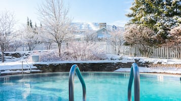 A swimming pool with metal railings, surrounded by snow-covered trees and a white picket fence.