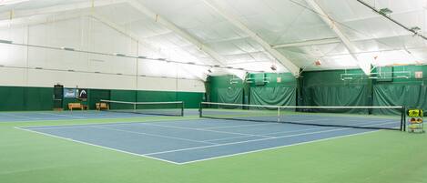 An indoor tennis court with a net, green walls, and a high ceiling.