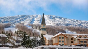A snow-covered town with a church featuring a clock tower, surrounded by buildings and a mountain in the background. - Long Trail House at Stratton Mountain Resort (Stratton)