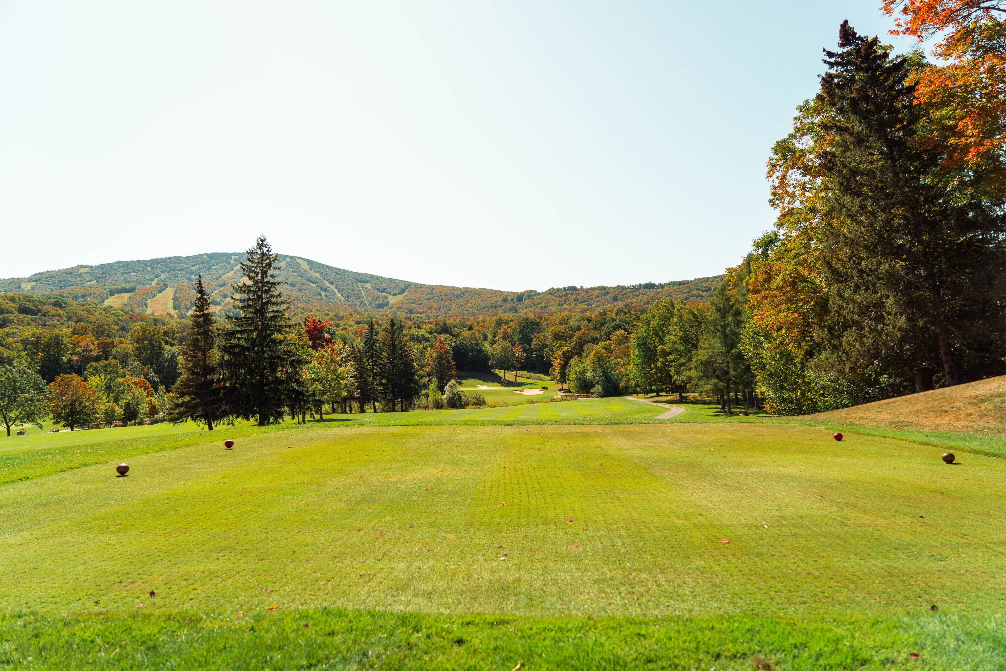 A golf course with a clear view of the fairway, trees, and distant hills.