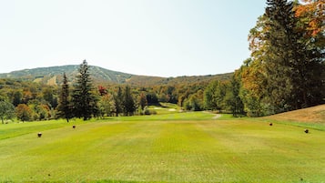 A golf course with a clear view of the fairway, trees, and distant hills.