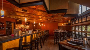 A bar area with wooden ceiling beams, bar stools, and a long counter with bottles and glasses. - Long Trail House at Stratton Mountain Resort (Stratton)