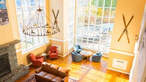 A spacious living room with a fireplace, leather sofa, and a large window offering a view of the outdoors. - Long Trail House at Stratton Mountain Resort (Stratton)