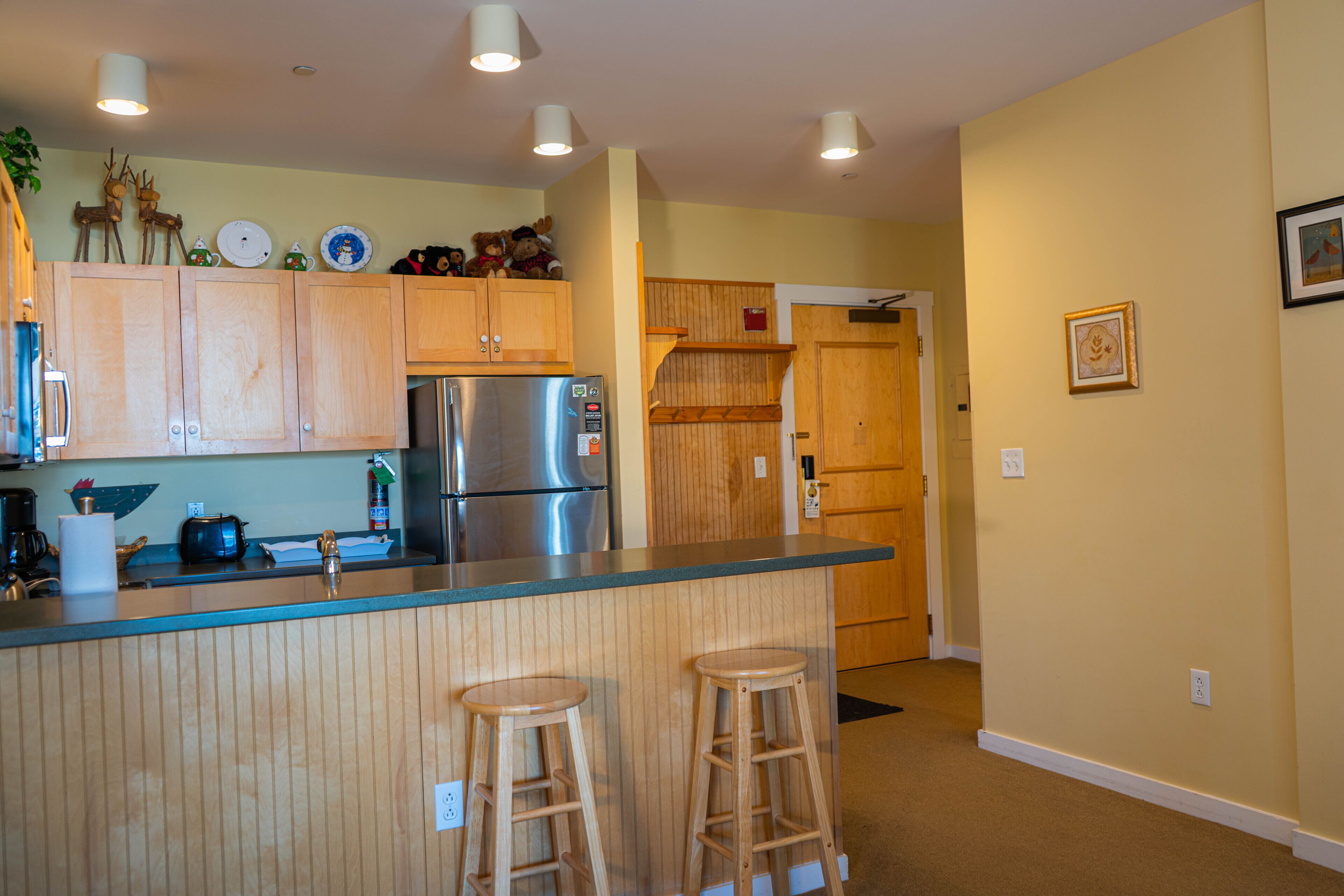 A kitchen with wooden cabinets, a stainless steel refrigerator, and two wooden stools.