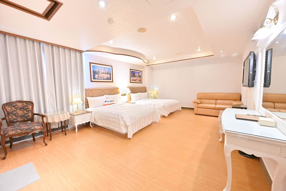 Quarto de hotel com cama grande, duas mesas de cabeceira, uma poltrona, um sofá e uma escrivaninha.