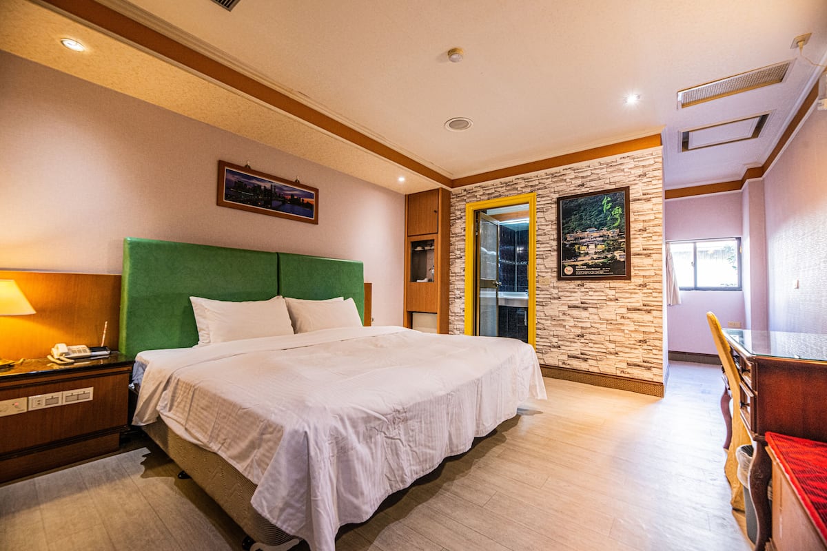 Quarto de hotel com uma cama grande, mesa de cabeceira, escrivaninha e uma cadeira.
