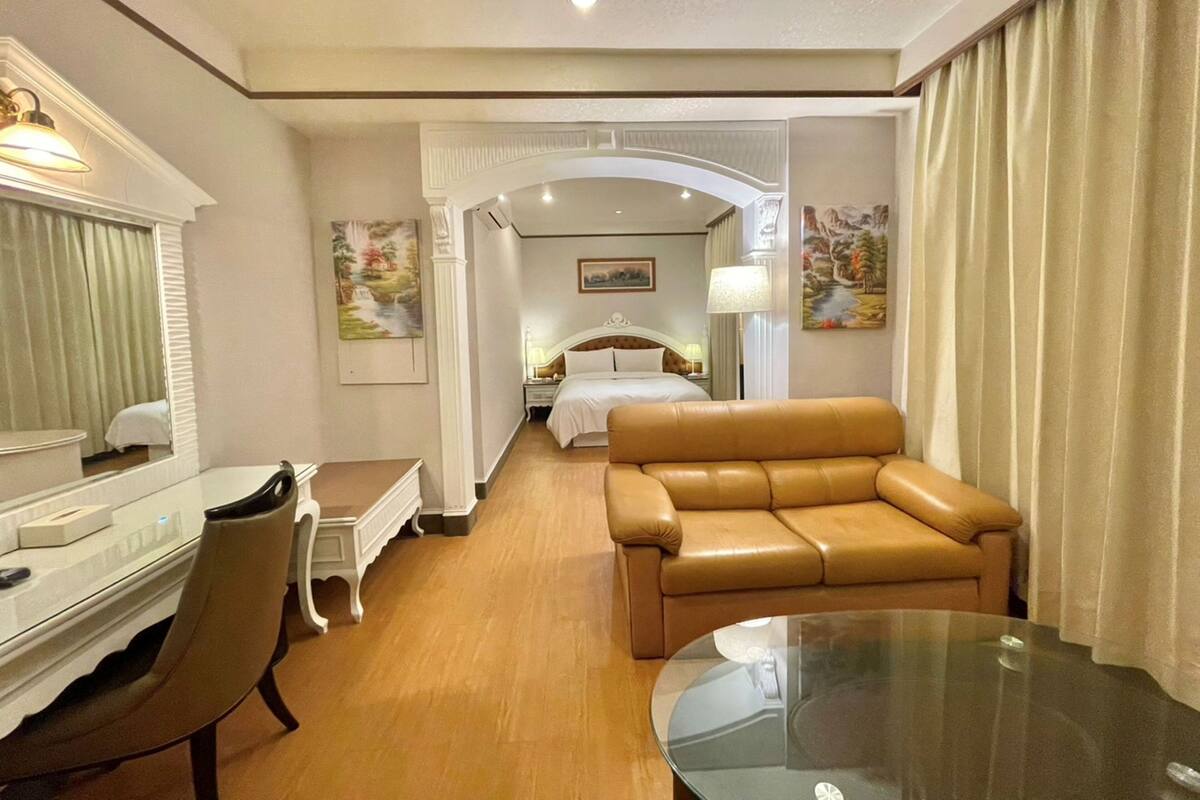 Quarto de hotel com cama, escrivaninha, cadeira, sofá de couro e mesa de vidro.