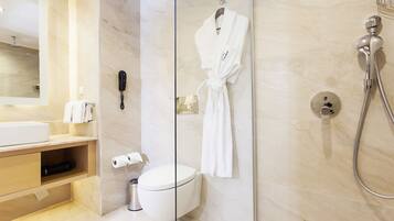 A modern bathroom with a glass shower enclosure, a white toilet, a vanity with a mirror, and a robe hanging on the wall.