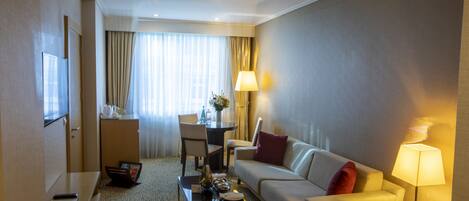 Una habitación de hotel con sofá, mesa de centro, televisión, escritorio y lámpara.