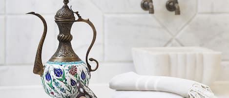 A bathroom with a white tiled wall, a decorative metal pitcher, a small bowl, and a towel.