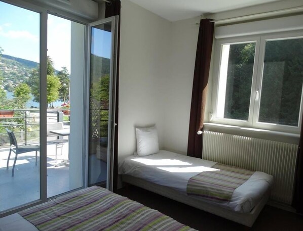 Una habitación pequeña con una cama, un ventanal y vistas a un balcón con mobiliario exterior.