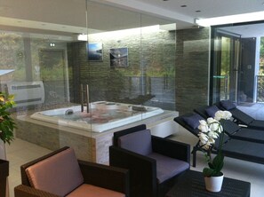 Un área de spa con un jacuzzi, sillones reclinables y una pared de vidrio con vistas.