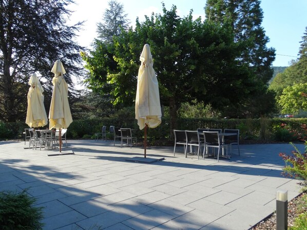 An outdoor seating area with tables and chairs, surrounded by trees and greenery. - Hôtel Restaurant l'Echo du Lac & Spa (Gerardmer)