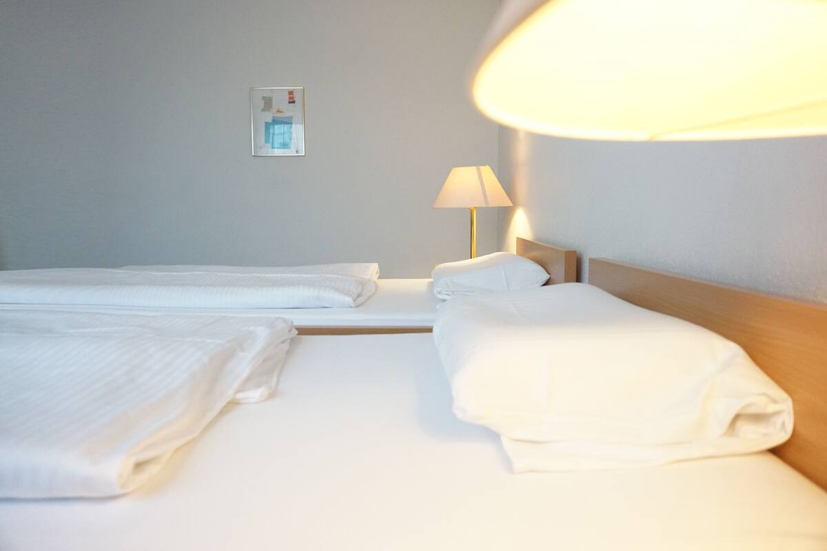Hotellihuone, jossa on kaksi sänkyä, yöpöytälamppu ja seinään asennettu valokytkin.