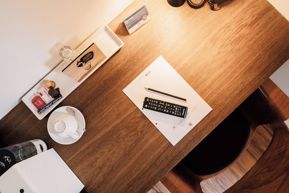 A wooden desk with a remote control, a cup, a spoon, a small box, and a calendar.
