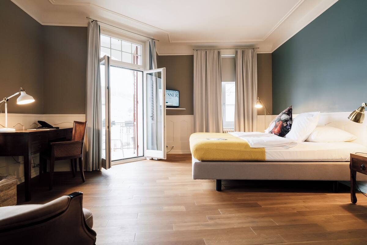 A hotel room with a bed, desk, chair, and a TV on the wall.
