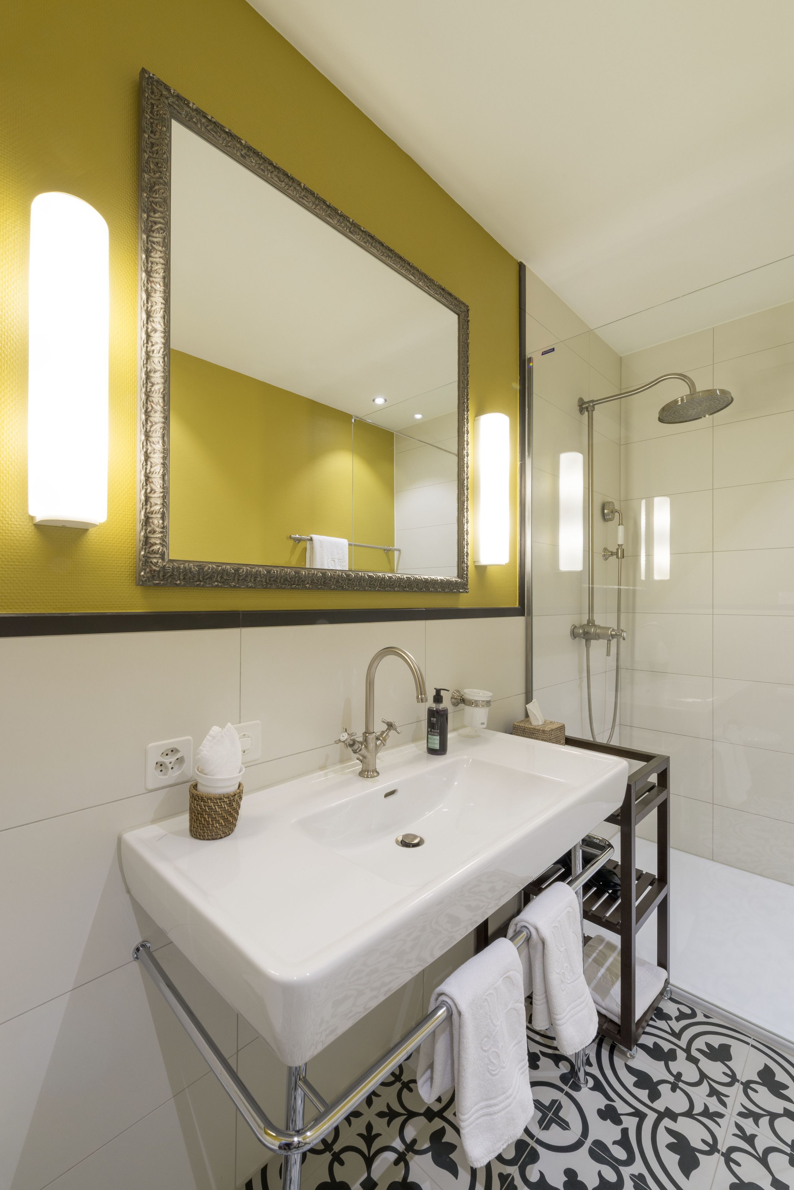 A bathroom with a large mirror, a sink, a shower, and a patterned floor.