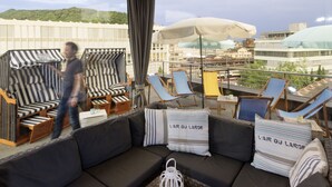 Eine Dachterrasse mit einer Sitzecke, gestreiften Stühlen und Sonnenschirmen.