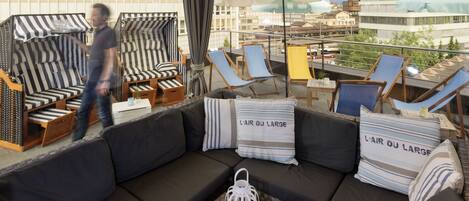 A rooftop lounge area with a sofa, striped chairs, and umbrellas.
