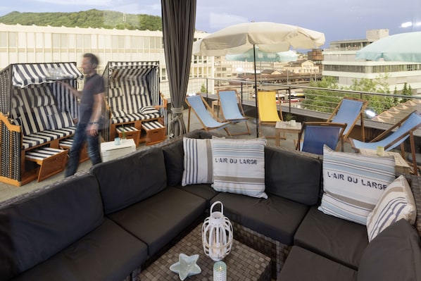 A rooftop lounge area with a sofa, striped chairs, and umbrellas. - Blue City Hotel (Baden)