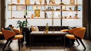 Ein modernes Wohnzimmer mit einem Ledersofa, zwei orangefarbenen Sessel, einem Holztisch und einem Bücherregal mit Büchern, Pflanzen und Dekorationsobjekten.