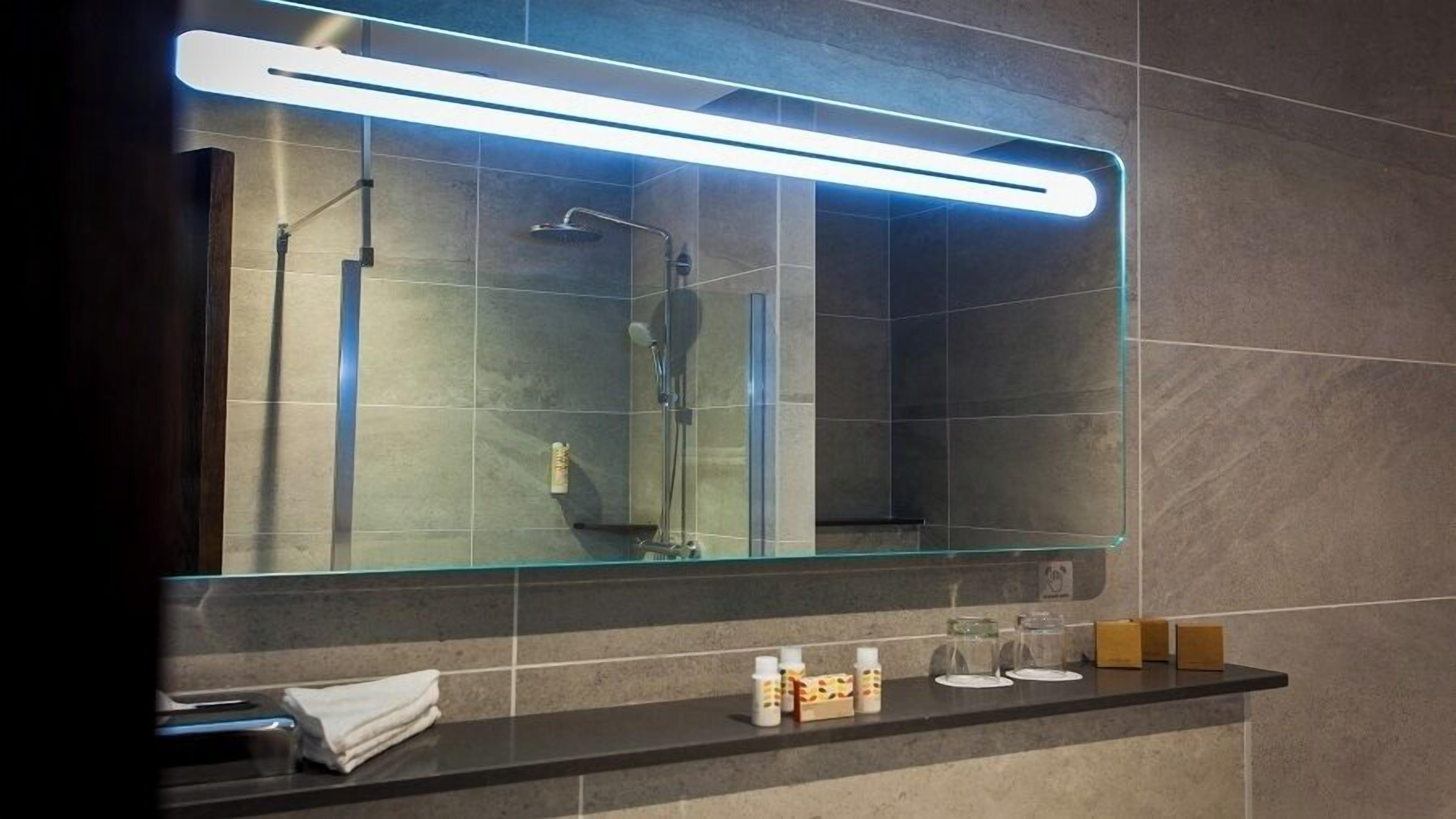A modern bathroom with a large mirror, a glass shower enclosure, and a vanity with toiletries.