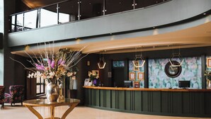 Un moderno vestíbulo de hotel con un mostrador de recepción, una mesa redonda de vidrio con un florero y un techo alto con lámparas colgantes.