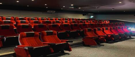 A cinema with rows of red and black seats, a dark ceiling, and a projector screen.