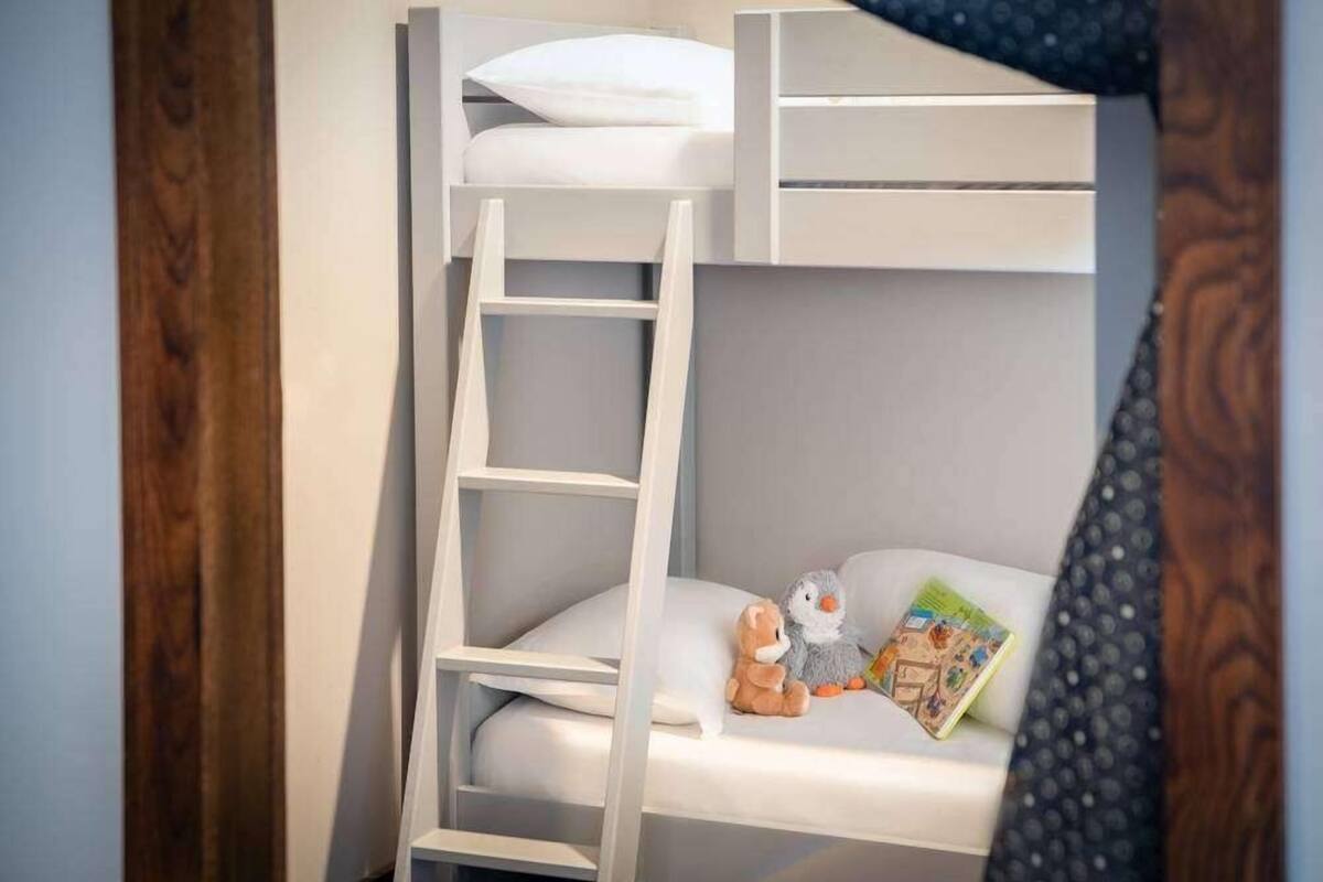 Ein Etagenbett mit einer Leiter, einem Kopfkissen und zwei Stofftieren auf der unteren Etage.