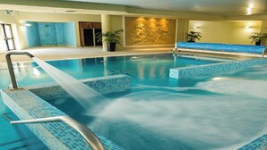 Una amplia piscina interior con agua cristalina, un área de jacuzzi y un mural en la pared.
