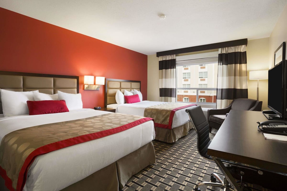 A hotel room with two beds, a desk, and a chair.