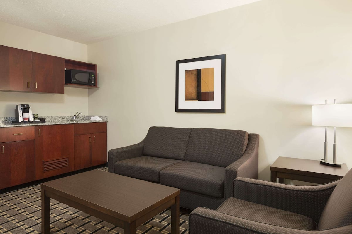 A hotel room with a kitchenette, a sofa, a small table, and a framed picture on the wall.