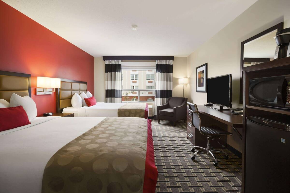 A hotel room with two beds, a desk, a chair, a television, and a refrigerator.