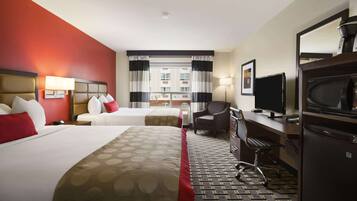 A hotel room with two beds, a desk, a chair, a television, and a refrigerator.