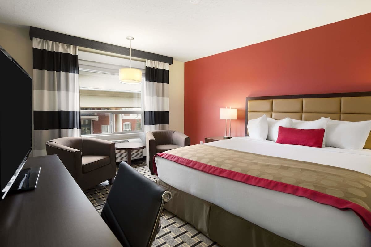 A hotel room with a large bed, a desk, a chair, and a window with curtains.