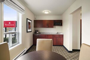 A hotel room with a dining table, a window with a view, a kitchen area with wooden cabinets, and a microwave.