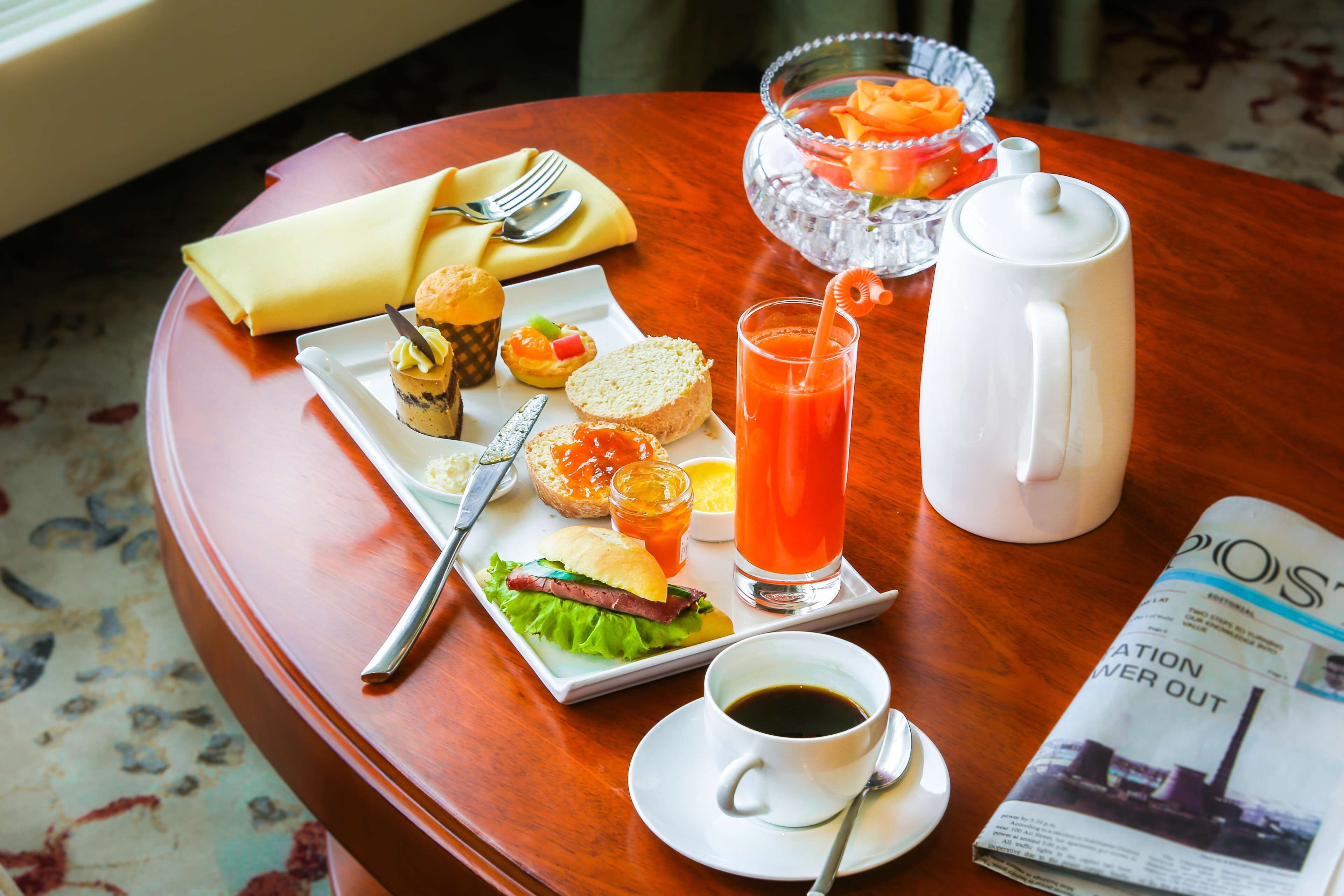 Un plateau de petit-déjeuner avec un sandwich, un muffin, du jus de fruits et du café, posé sur une table en bois.