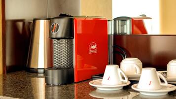 Una cafetera, un sistema rojo para preparar café y varias tazas blancas sobre una encimera.