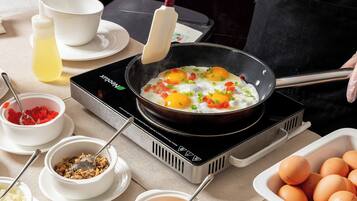 A kitchen with a frying pan on an induction cooktop, containing eggs and vegetables. There are bowls of ingredients and a container of eggs nearby.