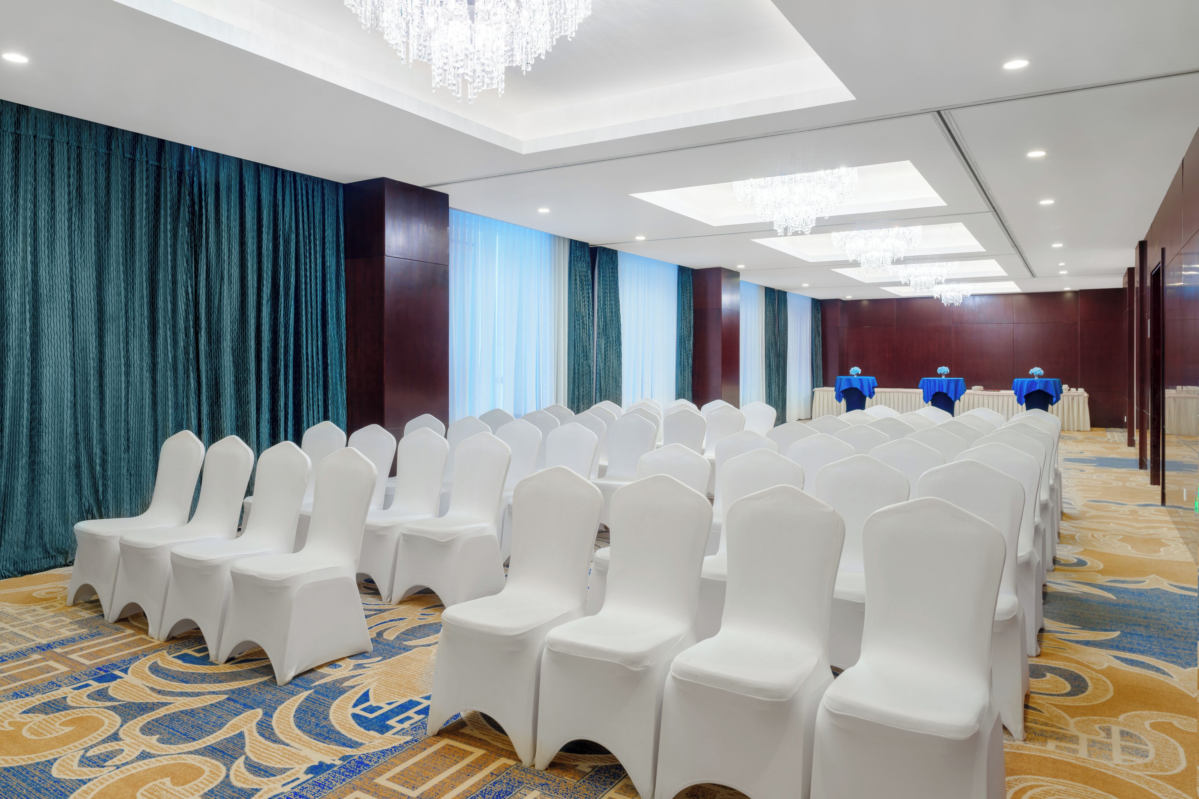 Un salón de conferencias con filas de sillas blancas, una alfombra estampada y una pared cubierta con telas azules y blancas.