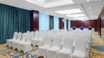 Un salón de conferencias con filas de sillas blancas, una alfombra estampada y una pared cubierta con telas azules y blancas.