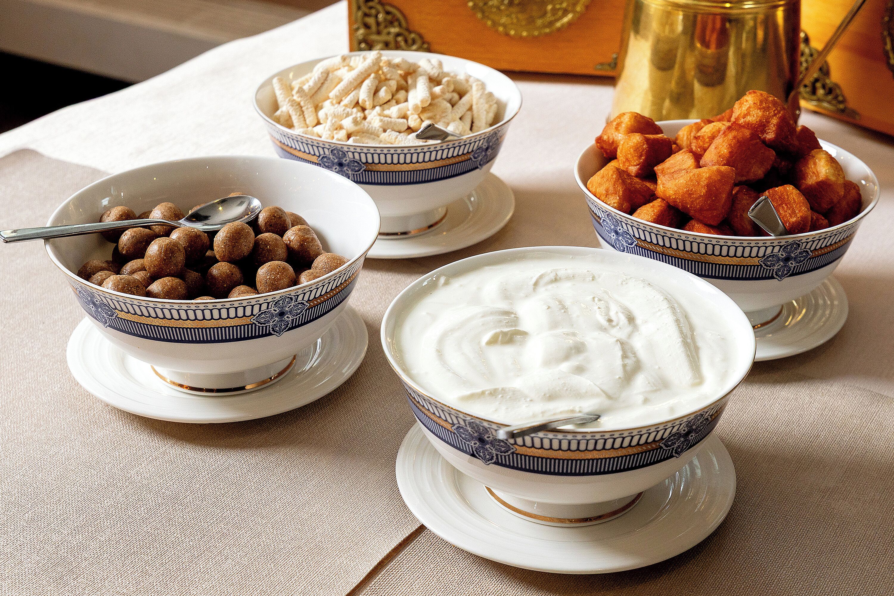 A table with four bowls of food, each with a spoon.