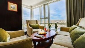 Un salon moderne doté d’une grande fenêtre, d’un canapé, d’un fauteuil et d’une table basse sur laquelle sont disposés des éléments pour le petit-déjeuner.