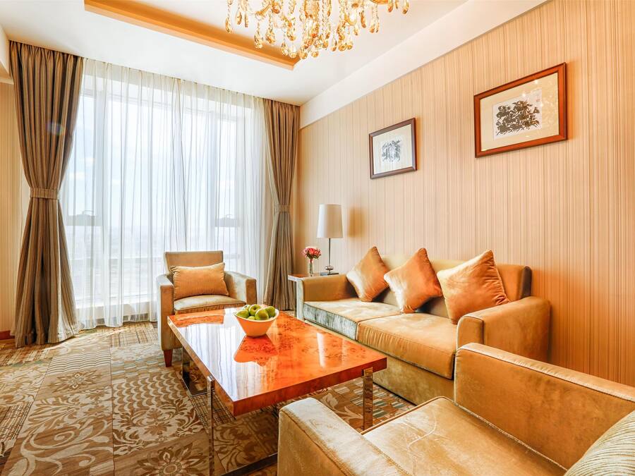 A modern hotel room with a sofa set, a wooden coffee table, and a patterned carpet.