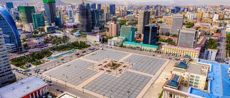 Una gran plaza con un monumento central, rodeada de edificios modernos y una calle concurrida.