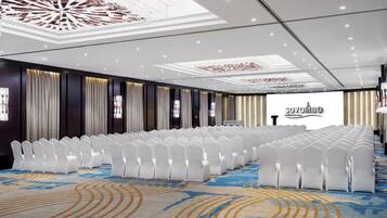 Un salón de conferencias con hileras de sillas blancas, una alfombra estampada y un techo con diseños elaborados.