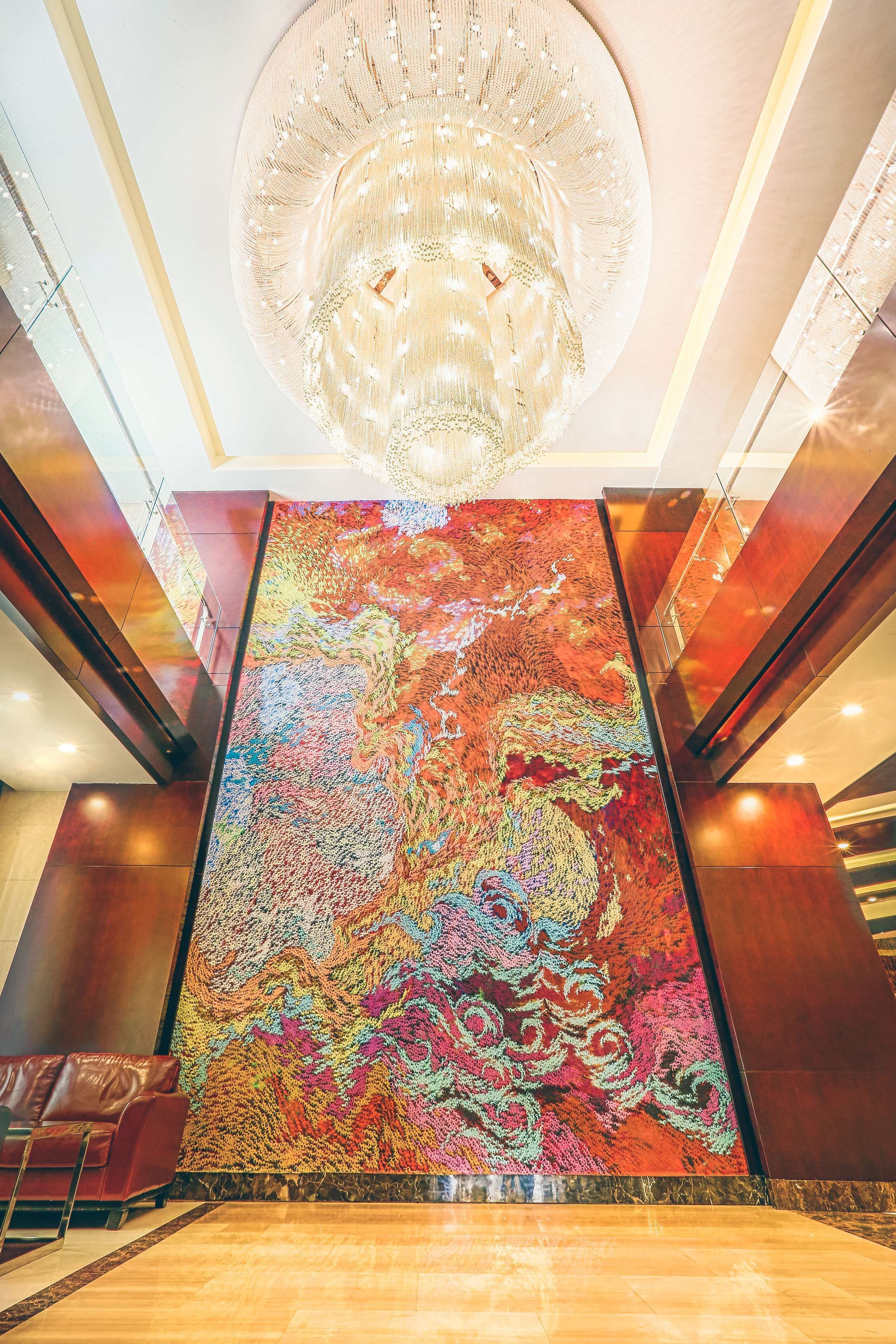 A grand lobby with a large, colorful abstract mural, a modern chandelier, and a spacious marble floor.