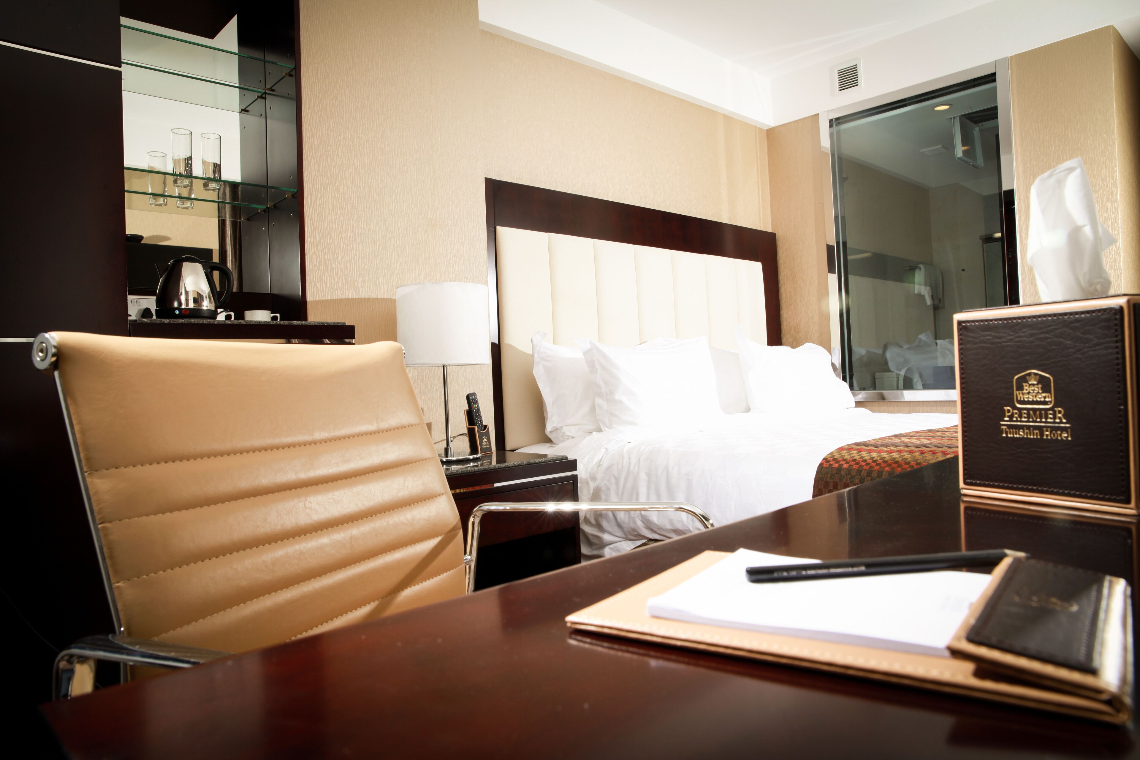 A hotel room with a bed, a desk, a chair, a bedside table, a lamp, a remote control, and a book.