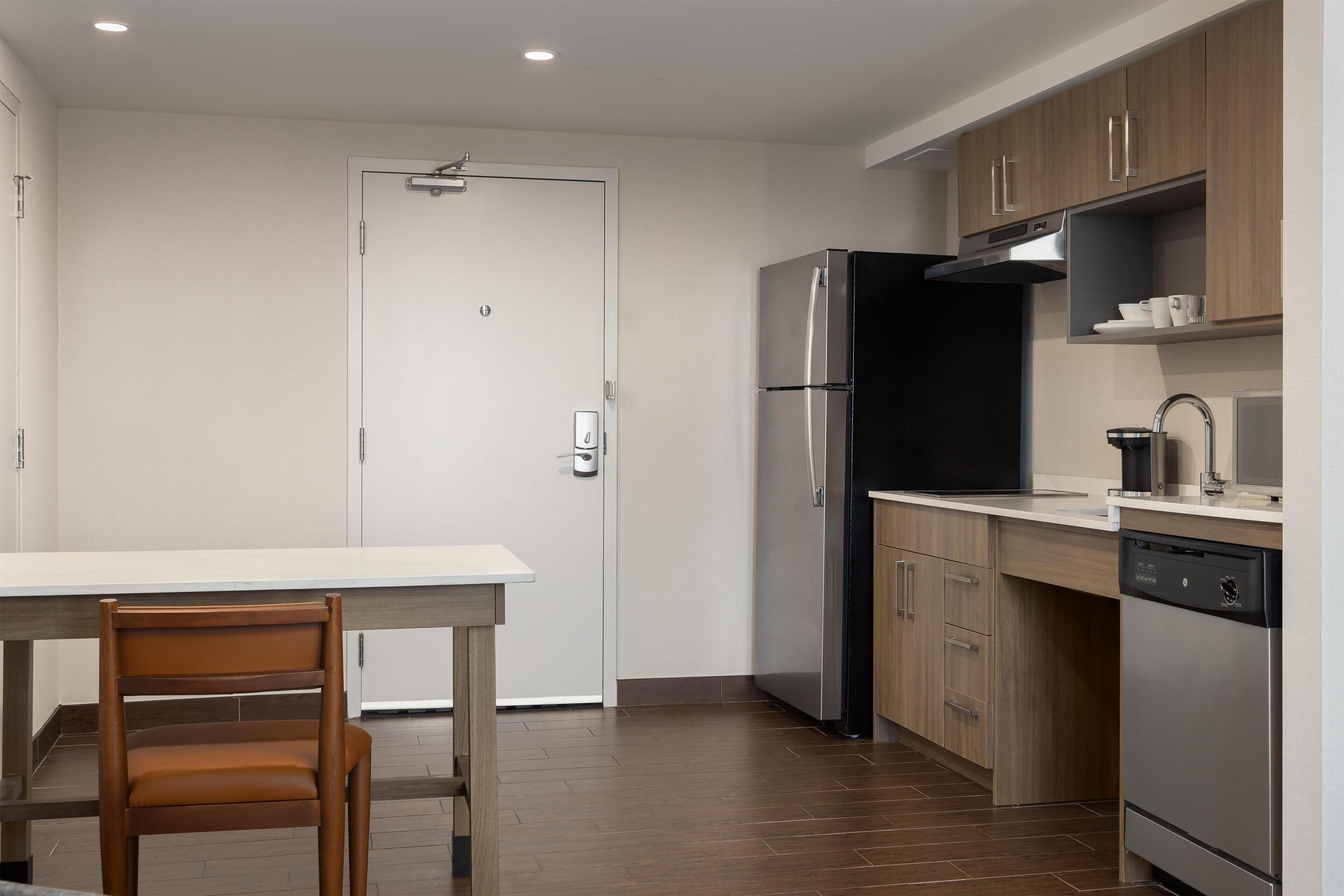 Una cocina moderna con un refrigerador de acero inoxidable, armarios de madera y una encimera blanca.