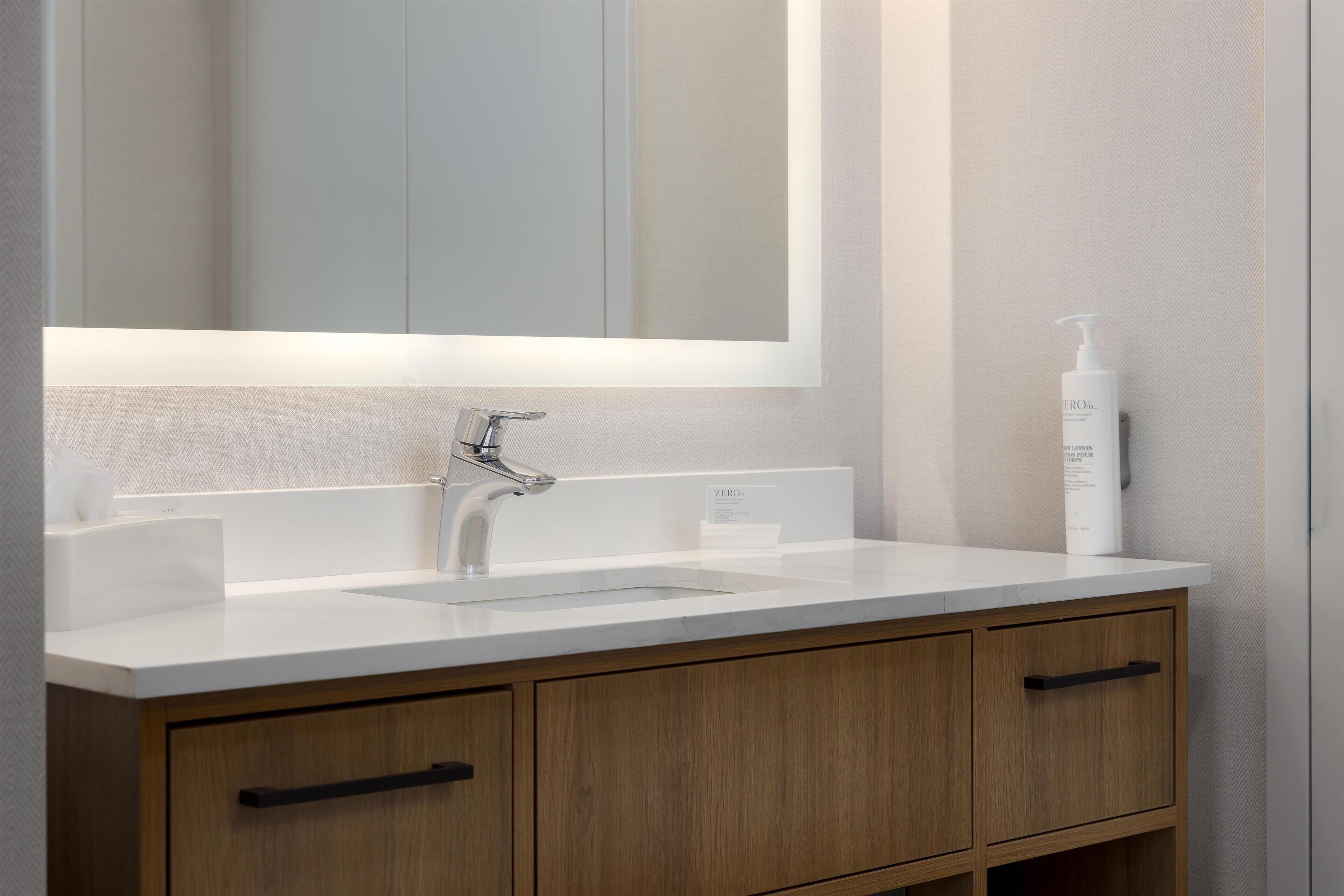 A modern bathroom with a white sink, wooden cabinets, and a large mirror.